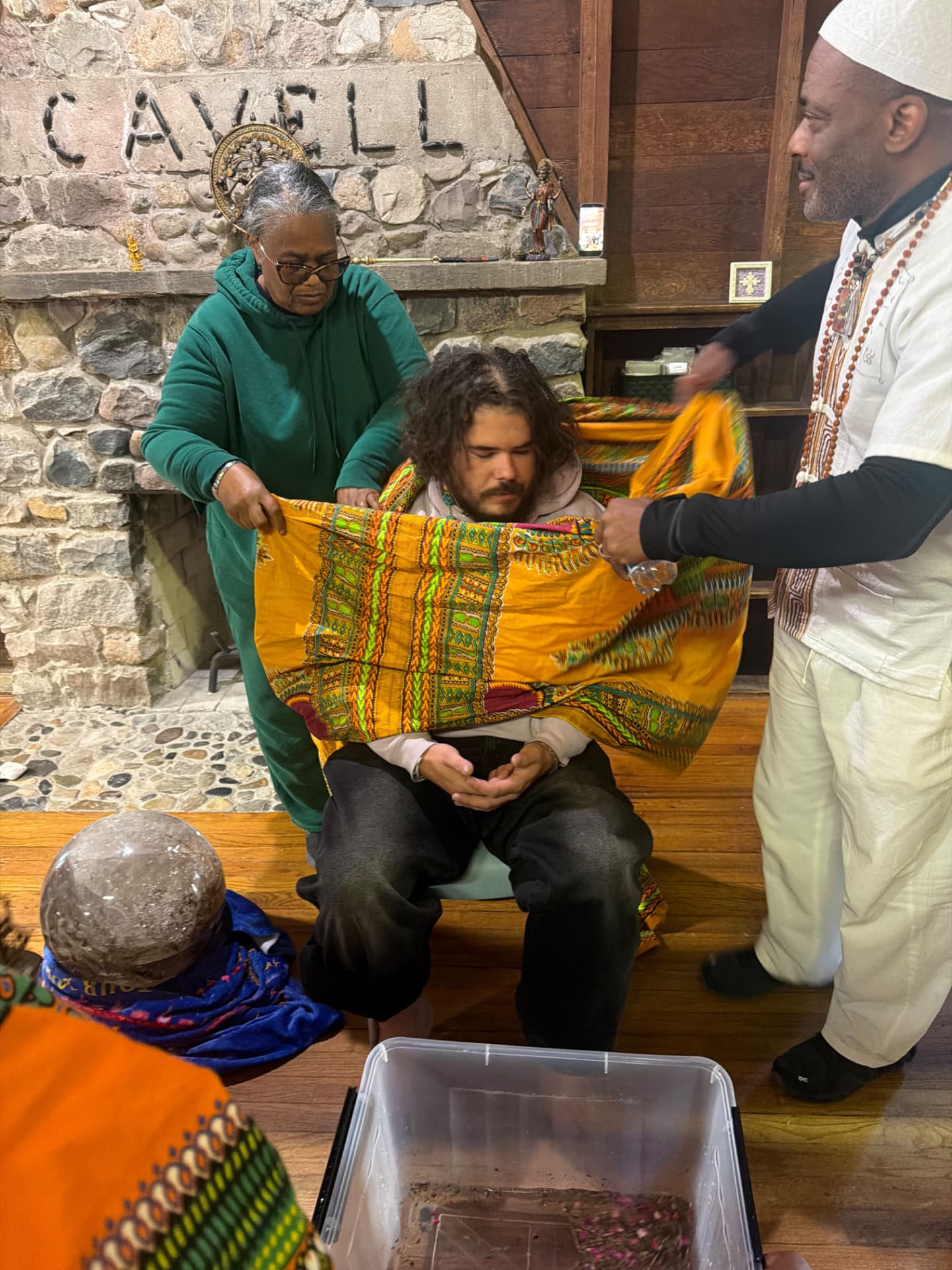 Facilitators wrap a participant in the golden cloth before the stone fireplace