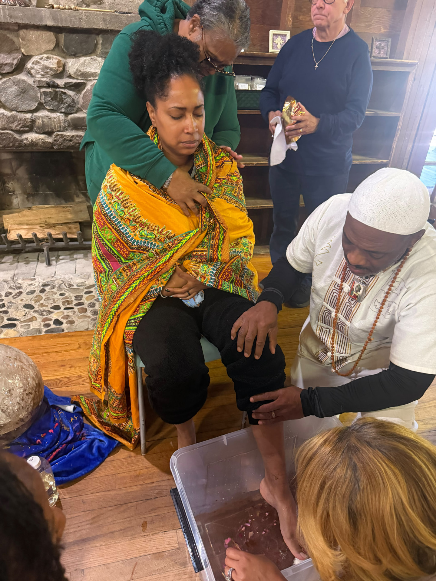 A facilitator kneels beside a seated participant during foot washing